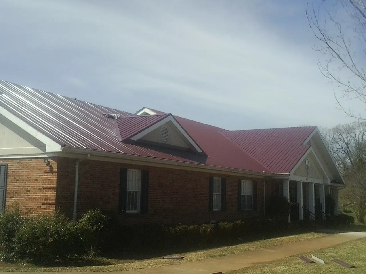 Red metal roof with gabled entries on a long brick building, from a Hail Damage Roof Repair job in Barwick