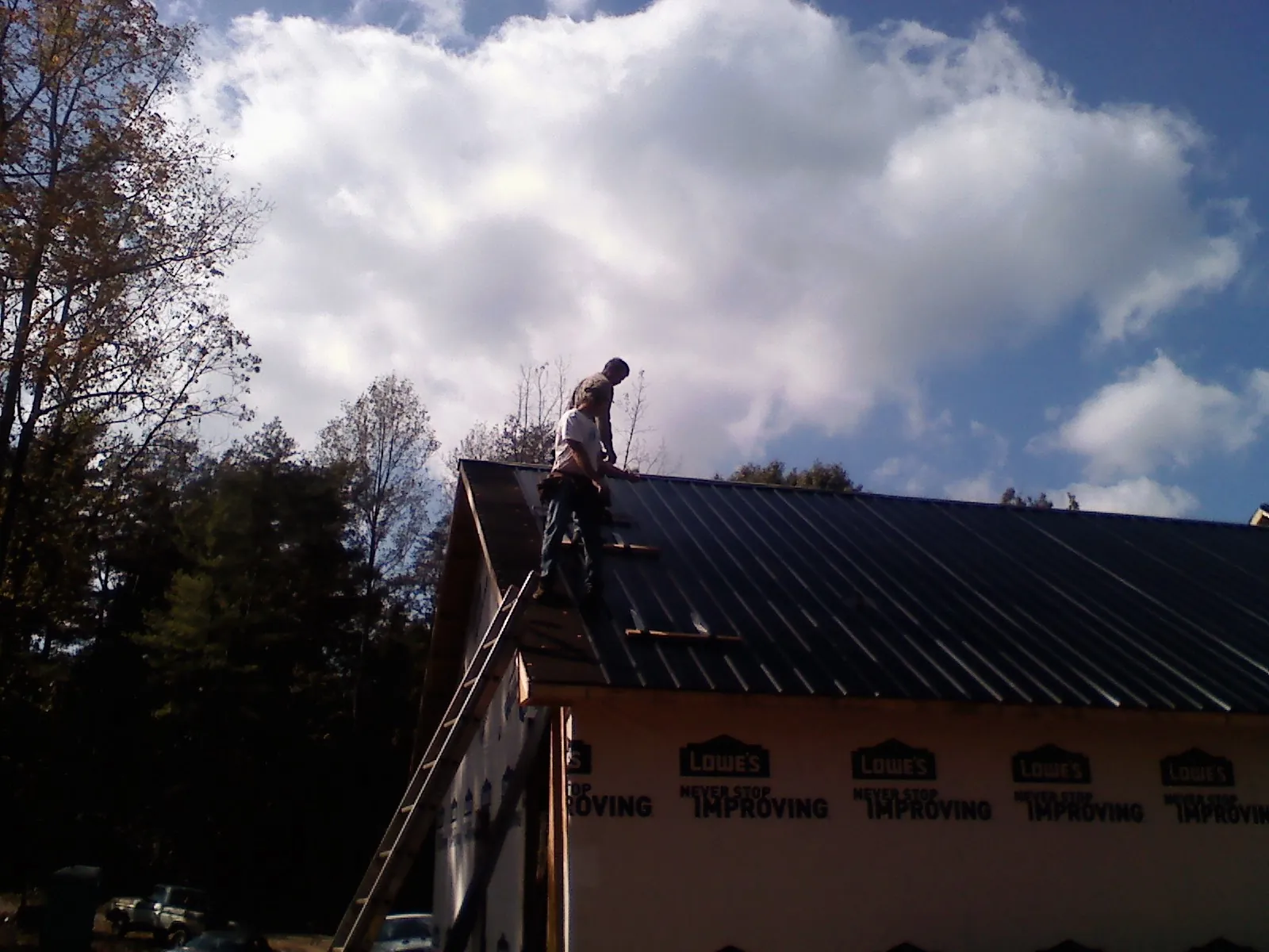 Roofer fastening dark metal panels high against a cloudy sky, from a Roof Inspection job in Barwick